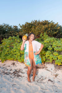 Woman on a beach holding a pineapple with greenery in the background wearing the Kaiso Shirt Dress Cover-up