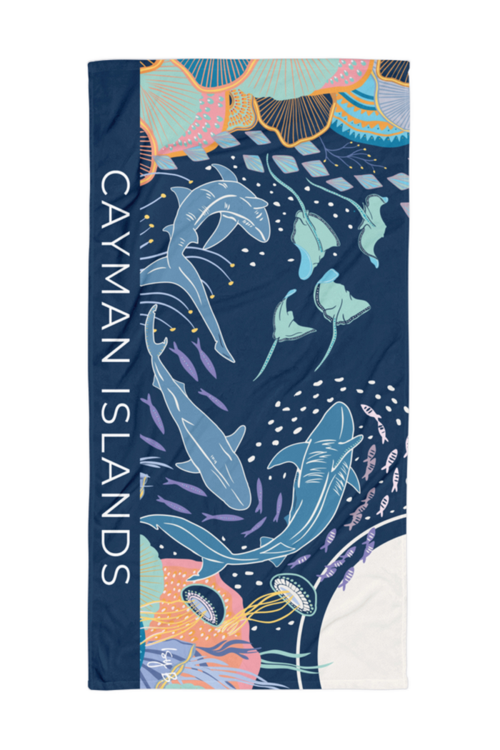 A rectangular beach towel featuring a colorful undersea design with sharks, jellyfish, and coral, plus the text 'CAYMAN ISLANDS' printed vertically on the left side.