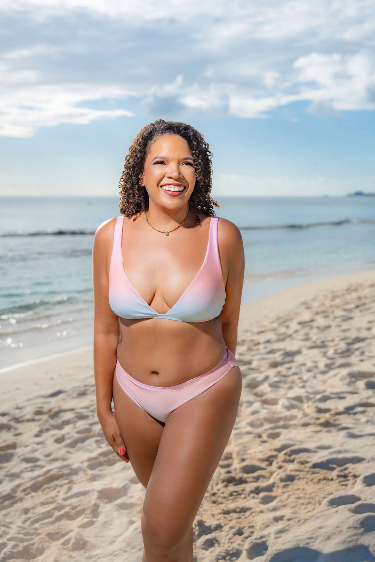 Woman in a pink and blue bikini standing on a beach with ocean and sky in the background